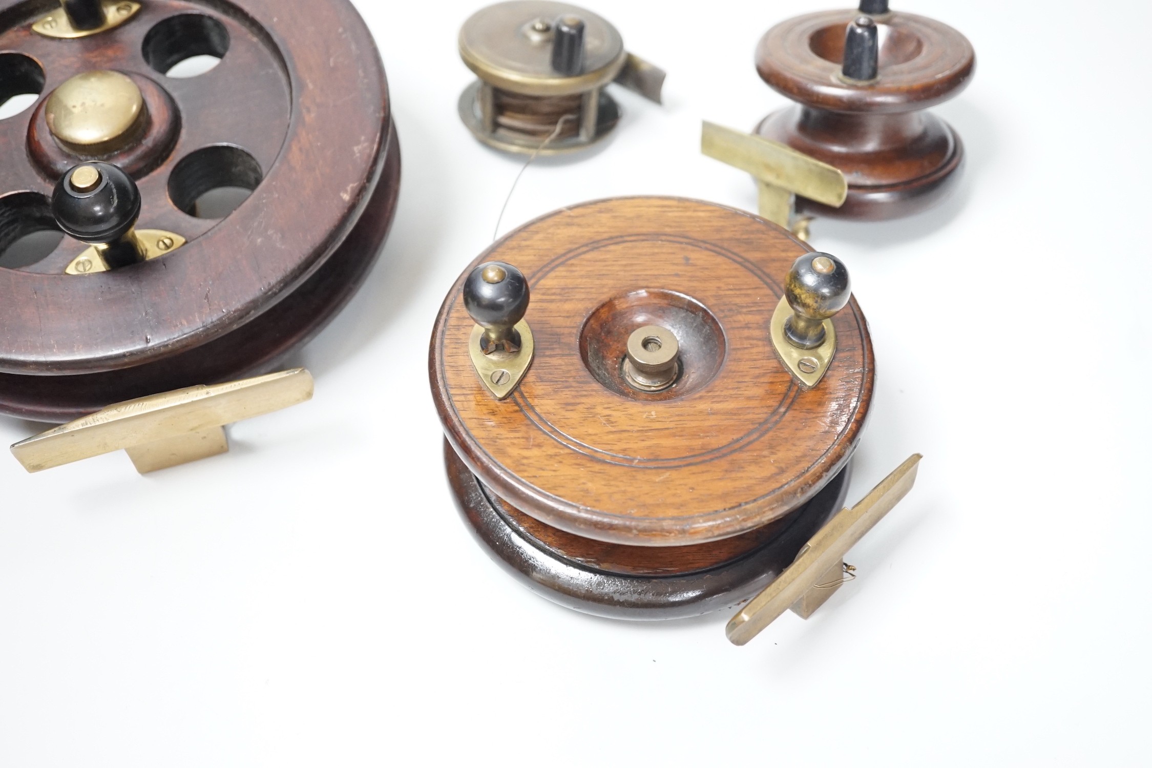 Three mahogany and brass fishing reels, largest 19 cm diameter and an Army & Navy brass reel, 6.3cm diameter